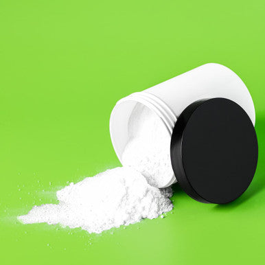 Spilled powder in a white container sitting next to a black lid on a green backdrop.
