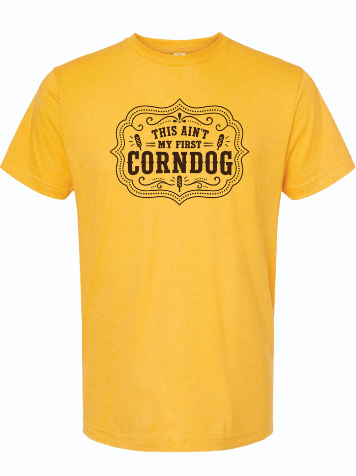 A yellow short-sleeve crewneck t-shirt with a black graphic print on the chest that reads 'THIS AIN'T MY FIRST CORNDOG' inside an ornate label design.